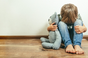 sad child with teddy bear in corner