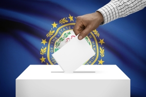 Person casting a ballot in front of NH flag
