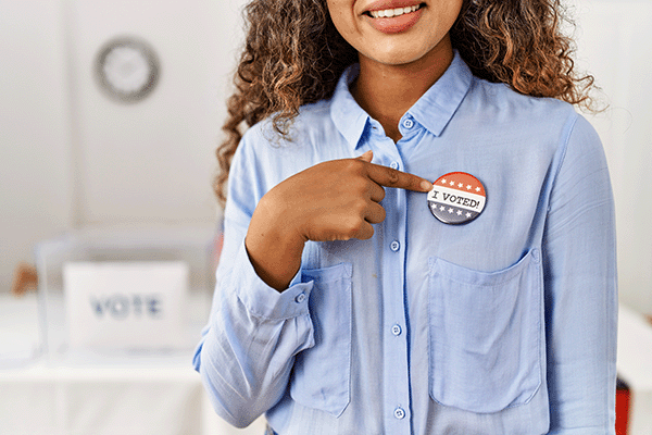 woman smiling pointing to I voted badge